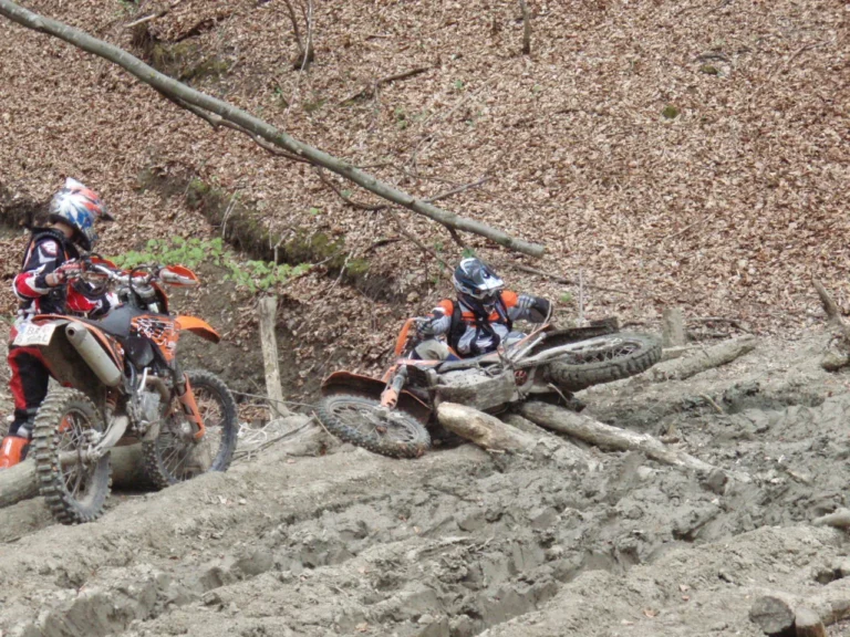 Zwei Enduro-Fahrer auf einem matschigen Waldweg mit Baumstämmen Zwei Enduro-Fahrer auf einem matschigen Waldweg mit Baumstämmen