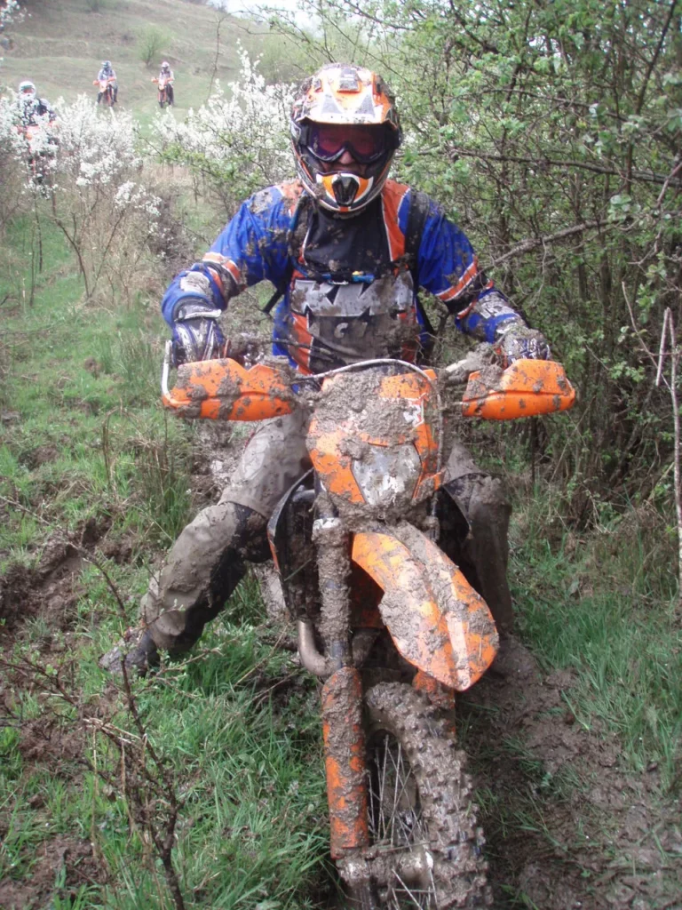 Schlammbespritzter Enduro-Fahrer auf KTM im Frühlingswald Schlammbespritzter Enduro-Fahrer auf KTM im Frühlingswald